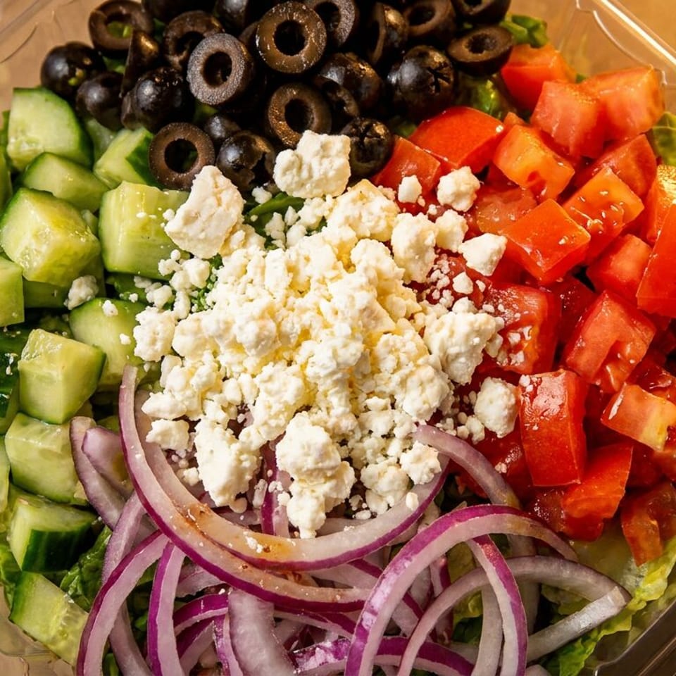 Fresh Greek salad with cucumbers, olives, feta, tomatoes, and red onions in a plastic container.